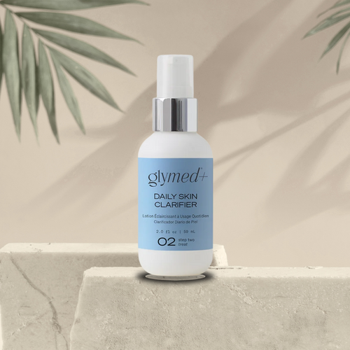 Glymed+ Daily Skin Clarifier bottle on a stone surface with a beige background and green leaves.