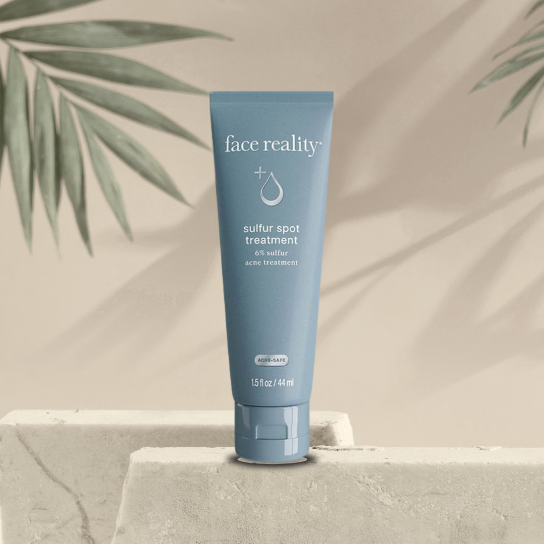 Blue tube of 'face reality' sulfur spot treatment on a neutral background with green leaves.