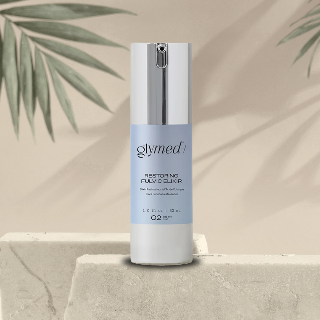 Skincare bottle labeled 'glymed+ restoring fulvic elixir' on a neutral background with green leaves.